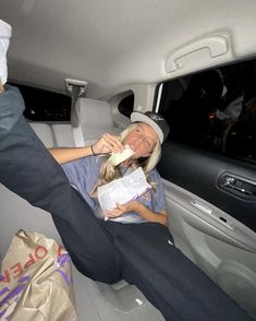 a woman is sitting in the back seat of a car eating something out of a paper bag