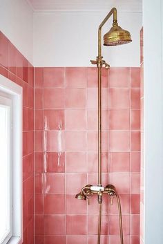 a pink tiled bathroom with gold fixtures and shower head in the corner, next to a window