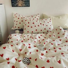 a bed with red hearts on it in a bedroom next to a painting and pillows