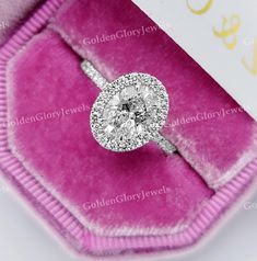 an engagement ring in a pink velvet box with a white diamond center and halo setting