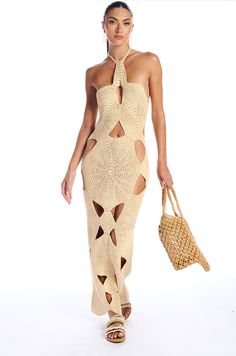 a woman is walking down the runway wearing a dress with cut outs and a straw bag