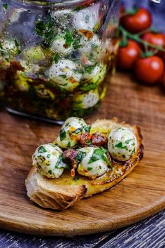 a wooden cutting board topped with bread covered in cheese and toppings next to tomatoes