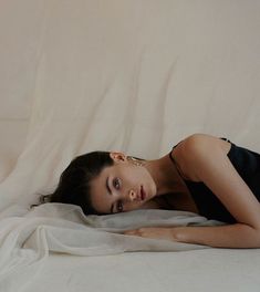 a woman laying on top of a bed under a white blanket with her eyes closed