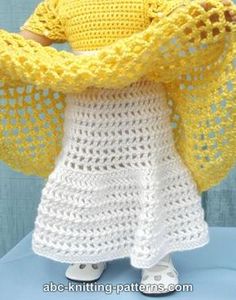 the doll is wearing a yellow knitted shawl over her shoulders and holding it with both hands