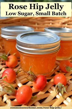 three jars of rose hip jelly sitting on top of a wicker basket with tomatoes