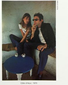 a man sitting next to a woman on top of a blue table in front of a white wall