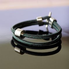 The TadBlu Naval Cord Men’s Cremation Bead Bracelet is a collection of cremation jewelry designed as an exquisite balance of a handsome, durable, and masculine design with a strong sense of elegance and beauty. The piece features a traditional naval rope in a combination of black and petrol green, which is braided and intertwined together to prominently display the dual-color combination. The colors pair perfectly with the 316 stainless-steel accents, one of which is a unique cylinder design tha Classic Green Adjustable Bracelet, Rope Braid, Masculine Design, Color Pairing, Cremation Jewelry, Memorial Jewelry, Cord Bracelets, Bead Bracelet, Rope Bracelet