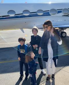 a woman and two children are walking towards an airplane on the tarmac while another child stands next to her