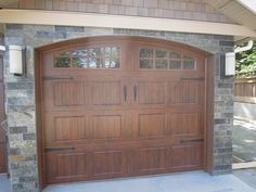 a brown garage door in front of a brick wall and stone pillars on the side of a house