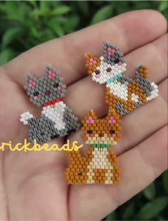 three small beaded cats sitting on top of each other in someone's hand