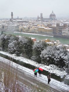 three people walking in the snow with umbrellas over their heads and buildings behind them