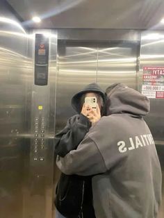 a man taking a selfie in front of a stainless steel elevator with his cell phone