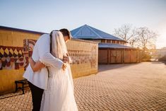 a bride and groom kissing in front of a brick wall with a mural behind them