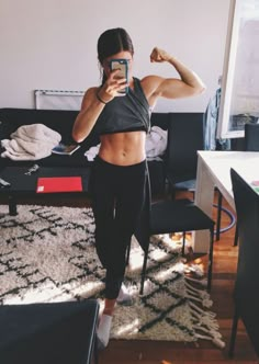 a woman taking a selfie with her cell phone in front of her, showing off her muscles