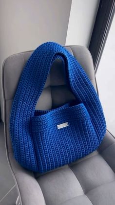 a blue knitted bag sitting on top of a gray couch next to a window