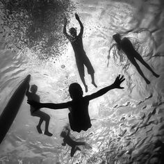 three people are swimming in the water with their arms out and one person is holding a surfboard