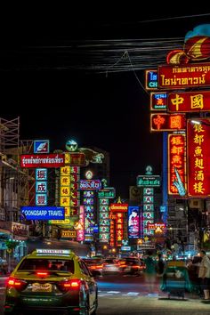 a busy city street at night with neon signs on the buildings and cars driving by