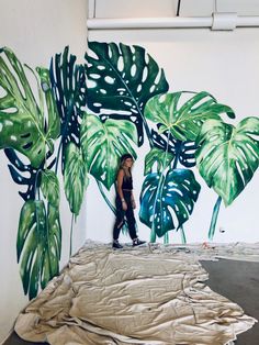 a woman standing in front of a painting with green leaves on the wall behind her