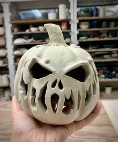 a person holding up a carved pumpkin in front of shelves with other items on it