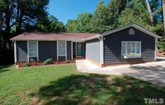 a gray house sitting in the middle of a yard next to some trees and grass