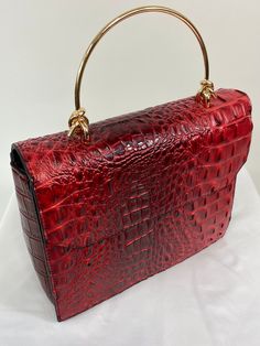 "Here we introduce to you the \"Clara\" Handbag, available in the fabulous shade of Red Velvet. This classy number which has a fabulous 1940s crocodile effect, has inside pockets and an inner zipped pocket. Use the delicate top handle or use the detachable shoulder strap to dress up or down your look ... with love from the UK x Features: Vegan Crocodile Print Leather made from PU and synthetic materials Cotton Lining Gold Knot hand bar Detachable shoulder strap Front flap opening Internal pockets /Security Zip Measurements in cms - 25.5cms x 20.5cms x 10cms (not including handle) Measurements in inches - 10\" x 8\" x 4\" (not including handle) www.classicbagsinbloom.co.uk Model - @retrofem" Red Top Handle Bag With Crocodile Pattern, Red Crocodile Pattern Shoulder Bag, Red Double Handle Bag With Crocodile Pattern, Evening Satchel Shoulder Bag With Crocodile Pattern, Formal Red Crocodile Pattern Shoulder Bag, Red Crocodile Pattern Shoulder Bag For Shopping, Handheld Evening Satchel With Crocodile Pattern, Red Crocodile Pattern Rectangular Bag, Chic Red Crocodile Pattern Bag