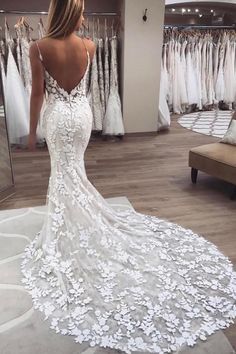 a woman in a white wedding dress looking at her gowns on hangers,