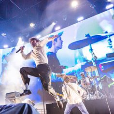 two men on stage with one holding a microphone and the other jumping in the air