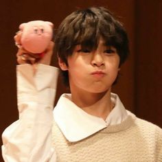 a young boy holding up a pink piggy bank in front of his face while wearing a white sweater