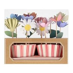 three pink and white striped cupcakes in a cardboard box with paper flowers on top