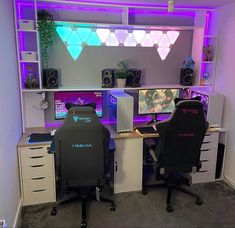 two computer monitors sitting on top of desks in front of a wall with purple lights