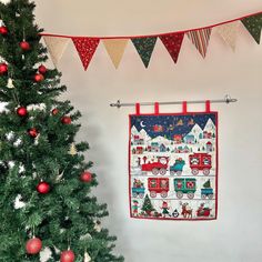 a christmas tree is next to a quilted wall hanging on a white wall with red and green decorations