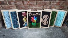 four framed art pieces with flowers and gears on them, sitting in front of a brick wall