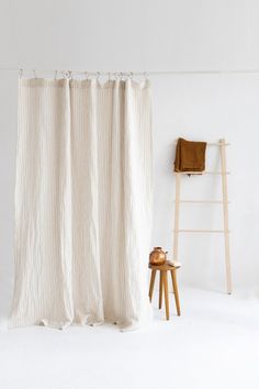 a white shower curtain sitting next to a wooden stool