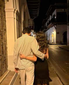 a man and woman walking down the street at night with their arms around each other