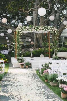 an outdoor wedding setup with white chairs and flowers on the aisle, surrounded by greenery