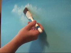 a hand is holding a paintbrush on a blue wall with clouds in the background