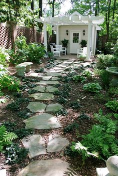 a stone path in the middle of a garden next to a white shed and trees