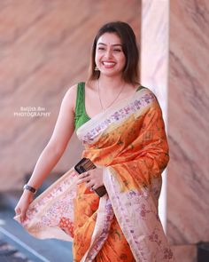 a woman in an orange and white sari smiles at the camera while standing outside