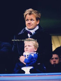 a man holding a small child in his lap at a soccer game with other people watching