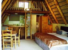 a room with a bed, table and ladder in it's center area next to a kitchen