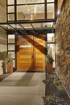 an entrance to a modern home with wood and glass doors, chandelier and potted plants