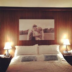 a bed with two pillows and pictures on the wall above it, along with lamps