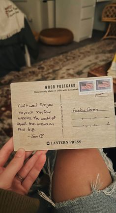 a person holding up a wooden postcard with writing on it's back and an american flag in the background