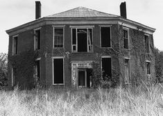 an old abandoned house with vines growing on it's roof and windows in the grass