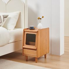 a wooden night stand sitting on top of a bed next to a vase with flowers