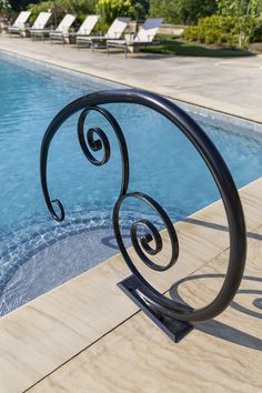 an iron spiral railing next to a swimming pool with lounge chairs in the back ground