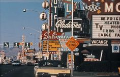 an old car is driving down the street in front of many signs and advertisements on buildings