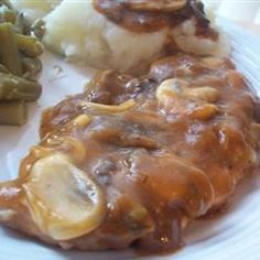 a white plate topped with meat covered in gravy next to green beans and potatoes