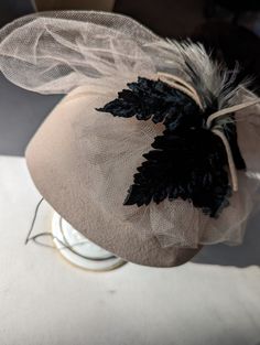 ".. UP for your consideration: a VINTAGE1940s women's gorgeous designer felted wool dress hat Fawn (tan) WITH BLACK TRIM featuring fascinator style work at top back/a star pattern of four velour leaves with feathers & fringe popping out, this elegant hat features the original veil (feels like silk) Label: ERNIE w/ the felt work marked Geo W Bollman & Co SIze: length: 6.75\"\": width:6\" height from brim to top:3\" on side 4\"at Front & back Vintage Beige Felt Hat For Winter, Elegant Beige Felt Hat For Winter, Elegant Beige Winter Felt Hat, Vintage Felt Hat For Fall Party, Vintage Felt Hat For Party In Fall, Elegant Cloche Mini Hat For Fall, Winter Evening Brimmed Fascinator, Vintage Fall Party Felt Hat, Elegant Fall Cloche Mini Hat