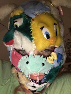 a woman wearing a dragon mask with other stuffed animals on her face and nose,